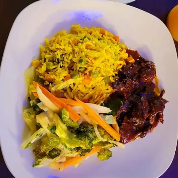 A Starving Vegan plate with yellow rice, mixed vegetables, and a dark saucy vegan protein.