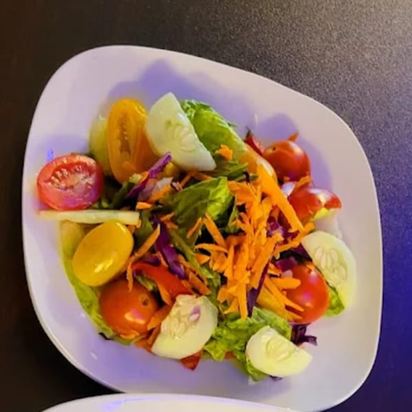 A colorful vegan side salad with mixed greens, shredded carrots, cucumbers, and cherry tomatoes.