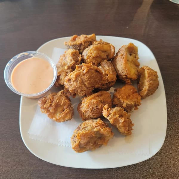 Crispy fried vegan nuggets with a side of creamy orange dipping sauce on a white plate.