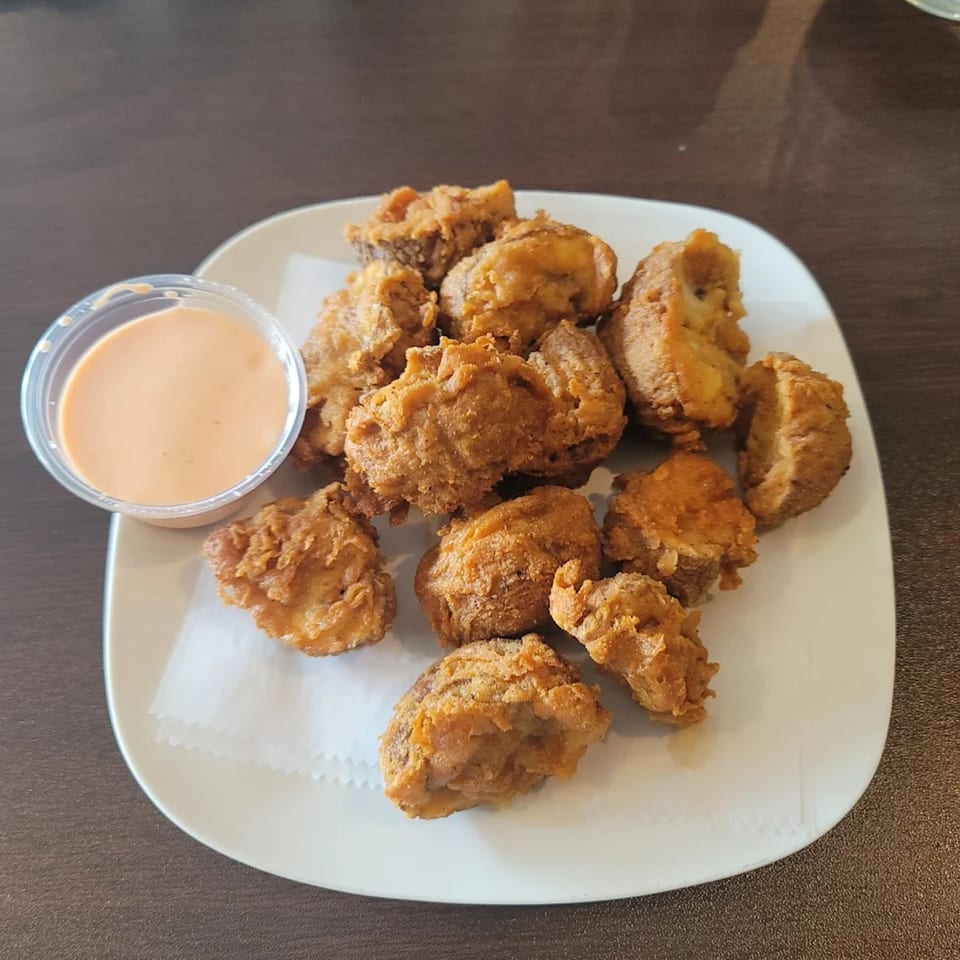 Crispy fried vegan nuggets with a side of creamy orange dipping sauce on a white plate.