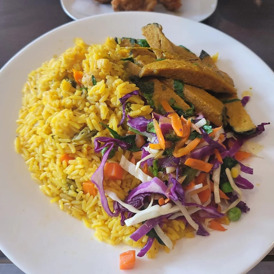 A Starving Vegan plate with yellow rice, seasoned plantains, and a colorful cabbage slaw.